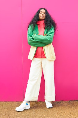 Young woman crossing her arms with a pink background, since she's an intense Cancer.