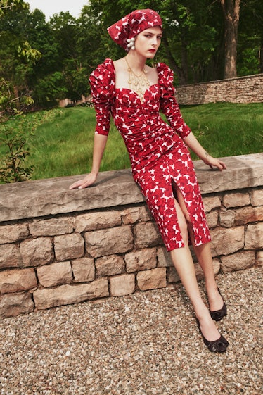 A female model posing while wearing a red Carolina Herrera dress and cap combination