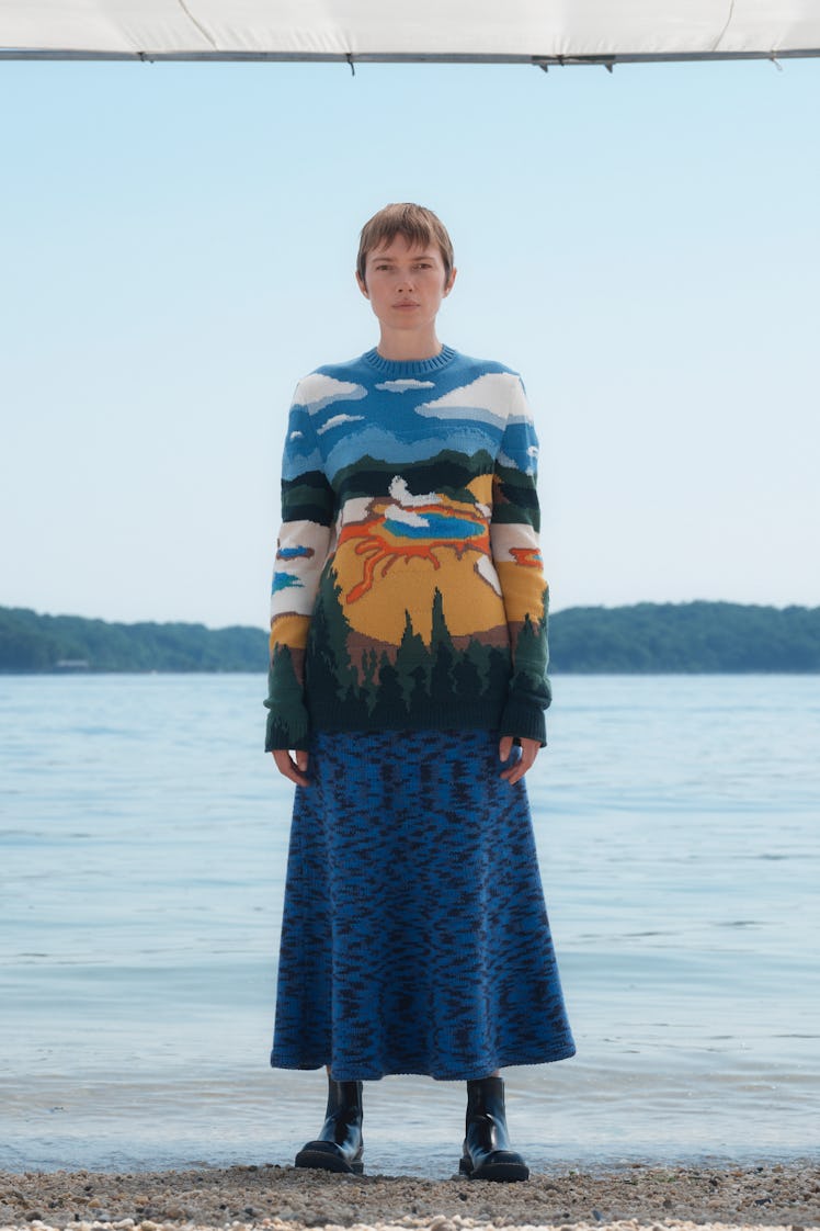 A female model posing in a Gabriela Hearst dress with a lake, wood, and sky drawing
