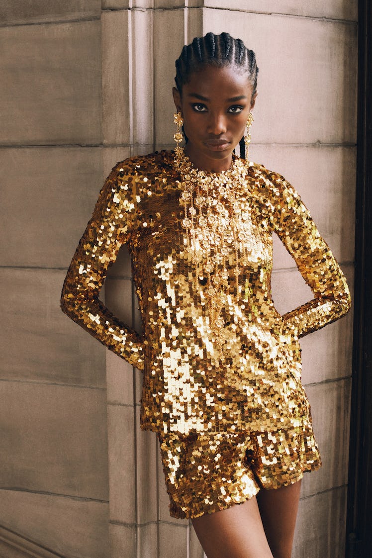 A female model posing while wearing a golden sequined Carolina Herrera dress