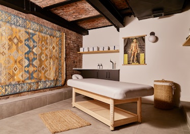 The massage room in the Bathhouse with a wooden massage table and colorful carped covering a brick w...