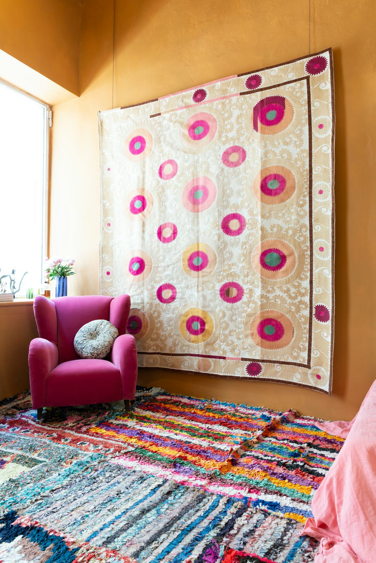 A Suzani from the 1960s hangs behind a pink velvet armchair from the ‘50s.