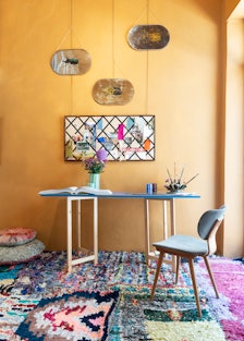 Over a patchwork of vintage rugs, a custom table and chair hold an array of Taschen books and cups b...