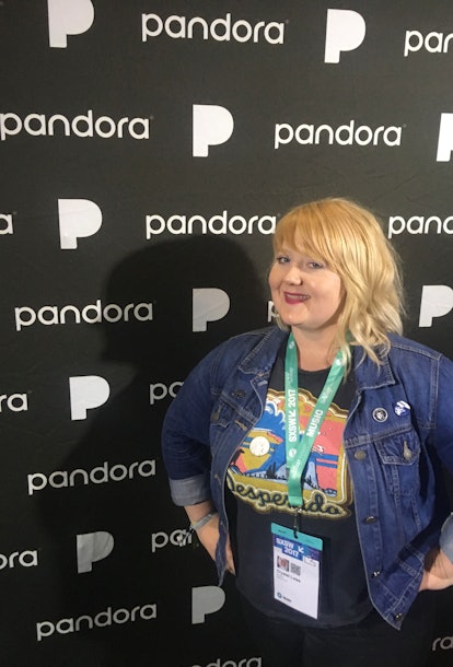 Crystal Lowe, wearing a band tee shirt and denim jacket, stands at a Pandora station at a music fest...