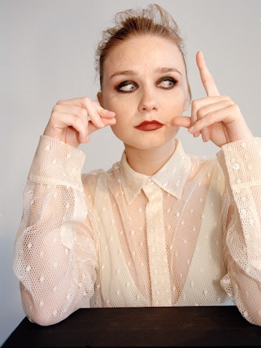 A portrait of Jessica Barden with smoky-eye makeup in a cream lace shirt