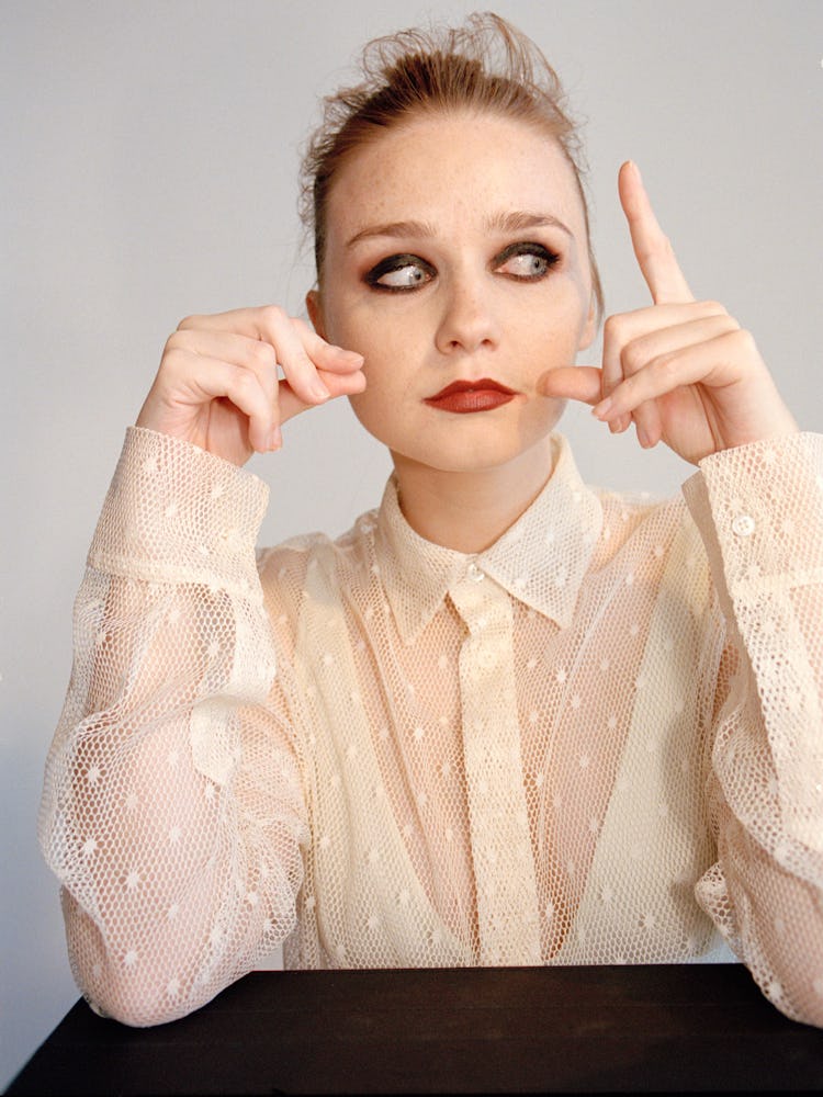 A portrait of Jessica Barden with smoky-eye makeup in a cream lace shirt