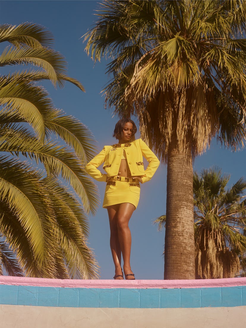 Taylour Paige standing outside in front of palm trees wearing a yellow matching Moschino jacket and ...