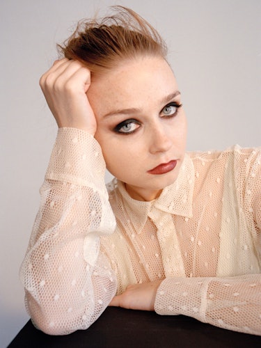 A portrait of Jessica Barden with smoky-eye makeup in a cream lace shirt