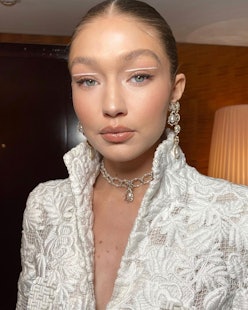 Gigi Hadid wears a beaded necklace and a white jacket in a selfie.