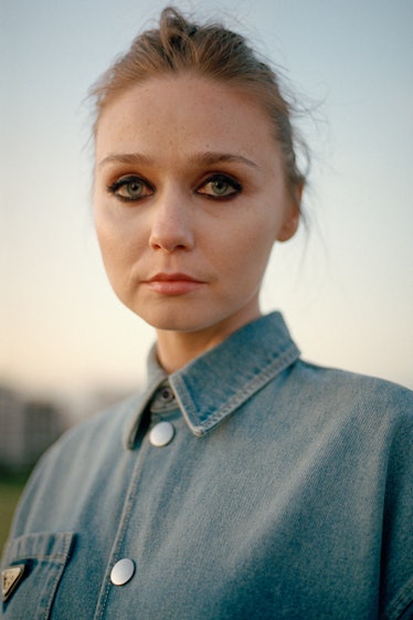 A portrait of Jessica Barden with smoky-eye makeup in a blue denim shirt