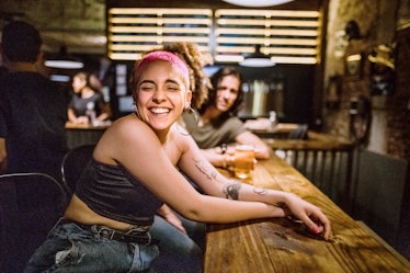 Young woman with pink hair, smiling in a bar, who's mentally younger than her real age, per her zodi...