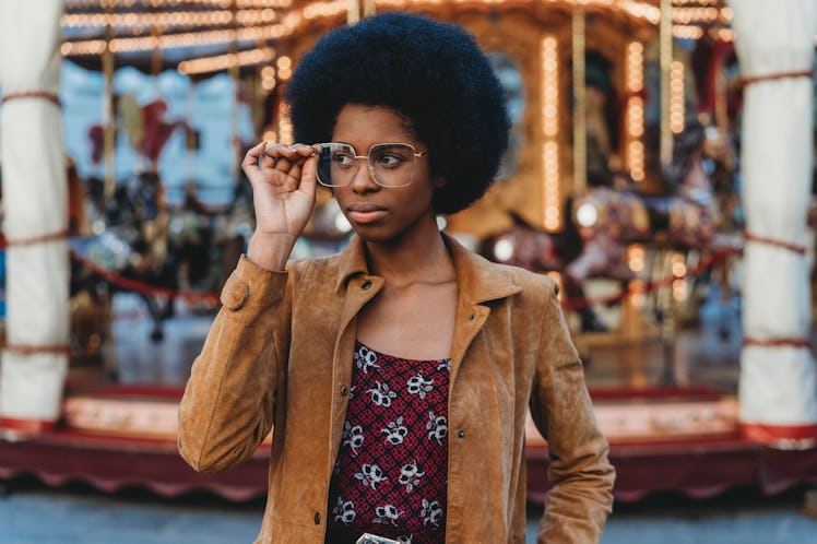 Young woman with glasses in front of a carousel, who's older & mentally more mature for her age, acc...
