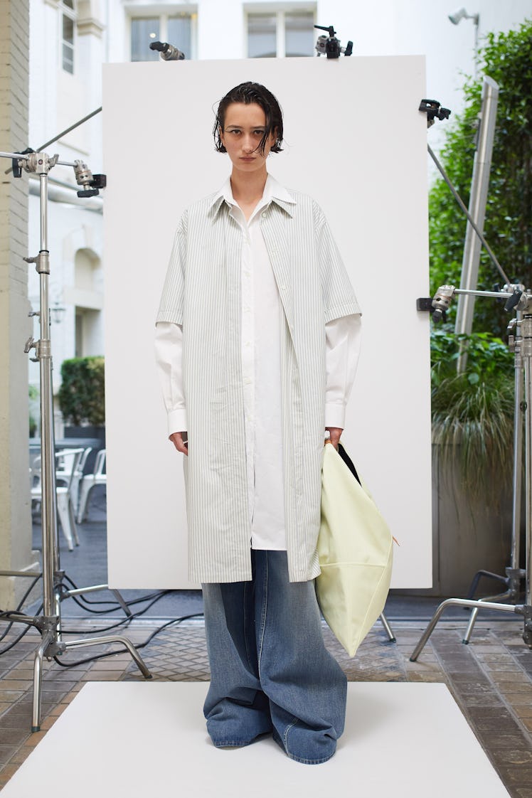A woman posing for a photo while wearing a white coat and baggy pants