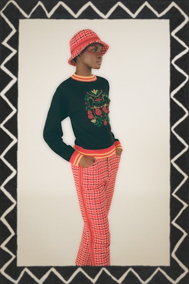 A female model wearing a red bucket hat, black shirt, and pink plaid pants