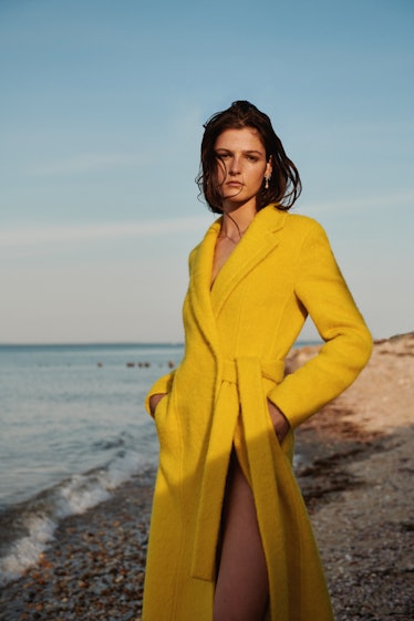A woman posing in a yellow coat while standing on a beach