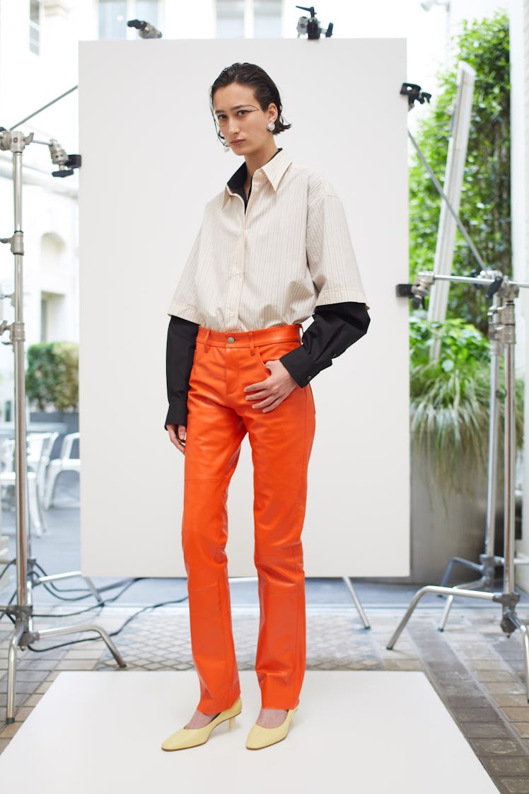 A woman posing in a white shirt and orange pants