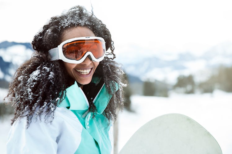 Young woman smiling in the snow, getting ready to snowboard before posting a picture on Instagram wi...