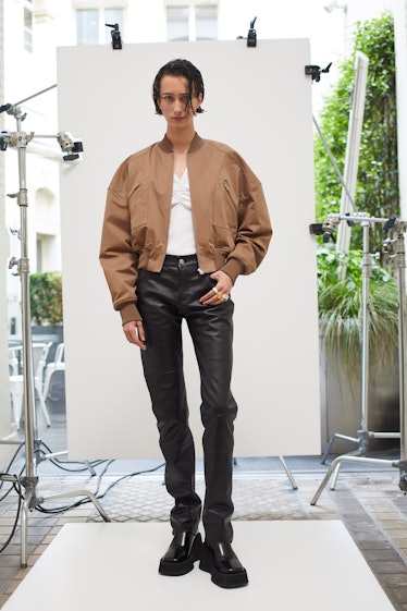 A man posing while wearing a brown jacket, a white shirt, and black pants