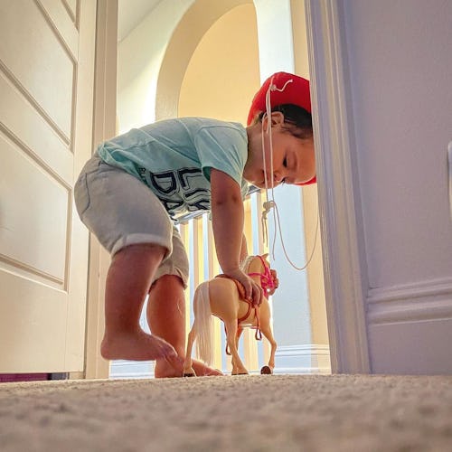 A little boy playing with a horse toy in the closet of his father