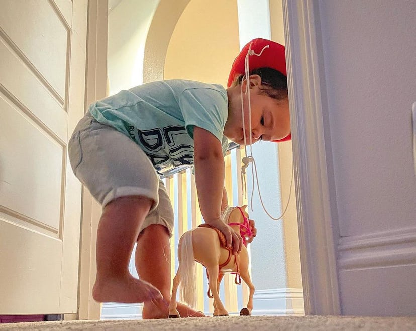 A little boy playing with a horse toy in the closet of his father