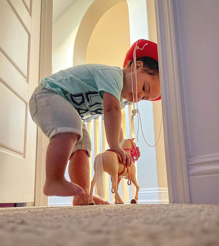 A little boy playing with a horse toy in the closet of his father