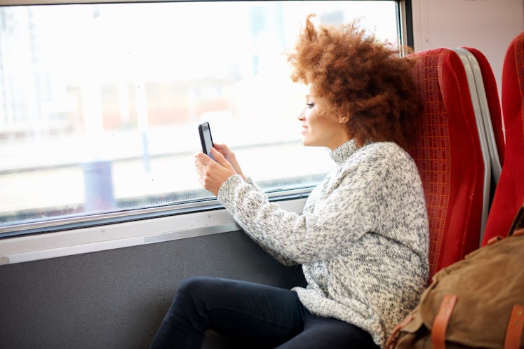 Young woman sitting on a train, taking a picture through the window before posting it on Instagram w...