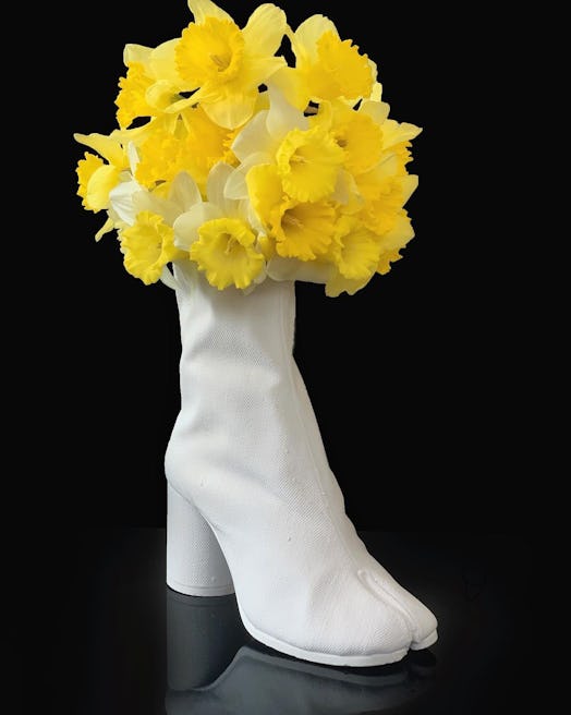 A white vase shaped like a boot filled with daffodils