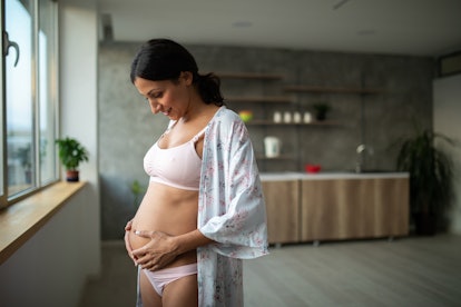 woman holding pregnant belly, feeling her baby kick