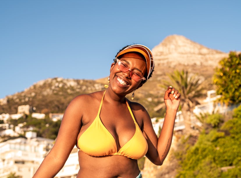 Young woman smiling on a beach vacation in a yellow bikini before posting a picture on Instagram wit...