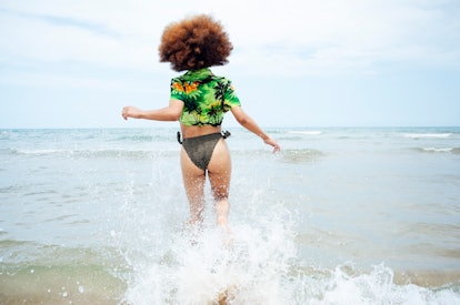 Young woman running into the water on the beach before posting a picture on Instagram with a tropica...