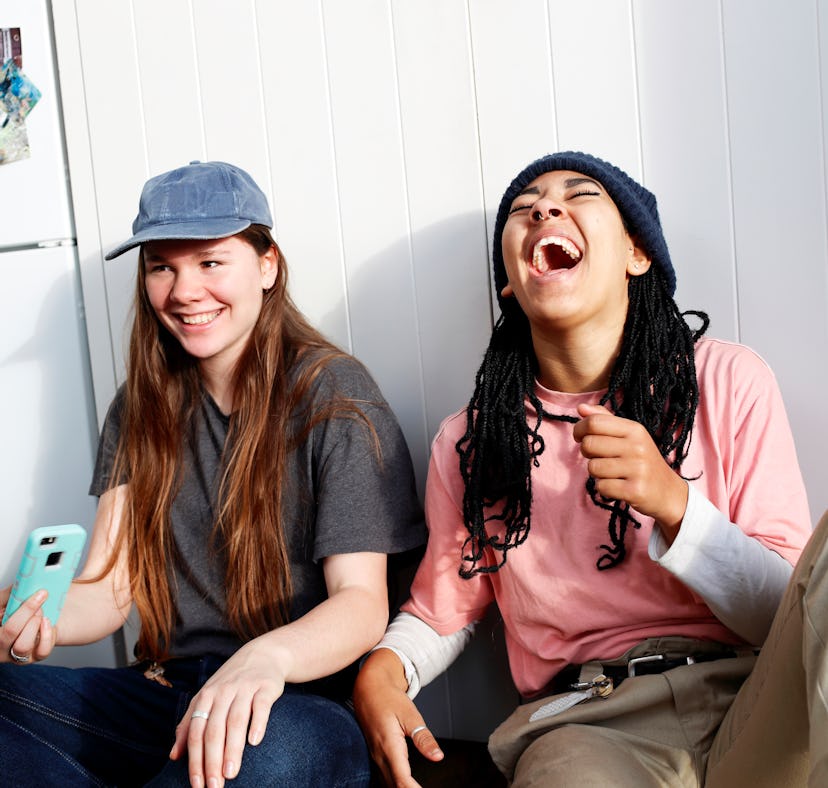 Young women holding phone, commenting funny captions on their friend's Instagram posts.