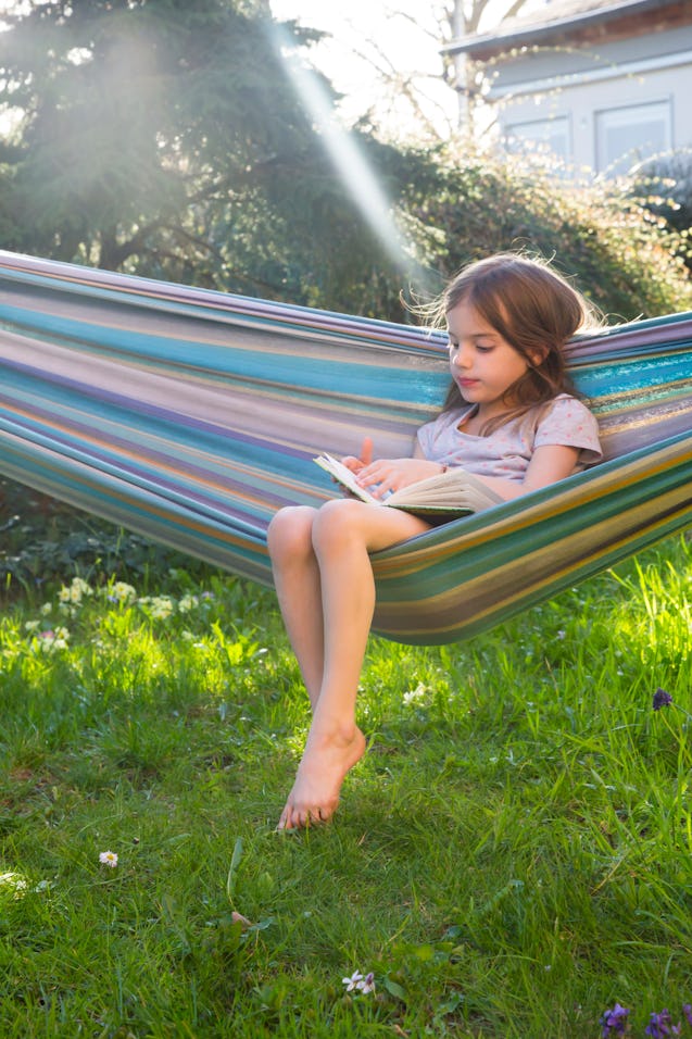 Little girl sitting on hammock in the garden reading a book