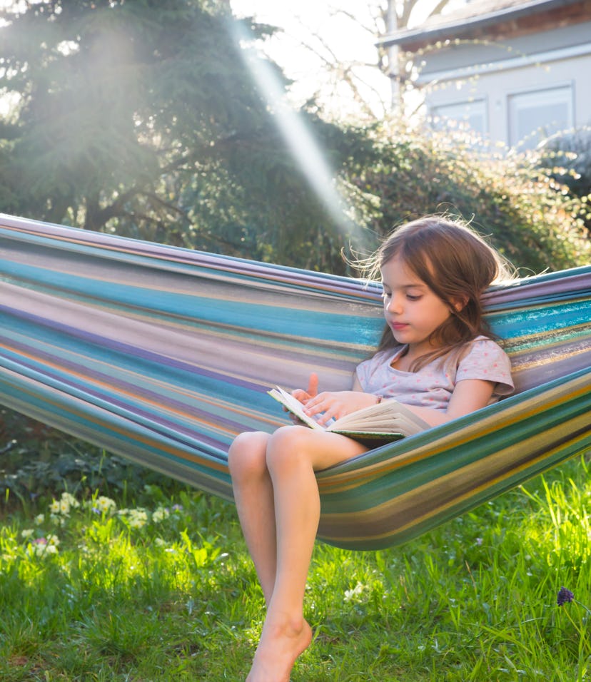 Little girl sitting on hammock in the garden reading a book