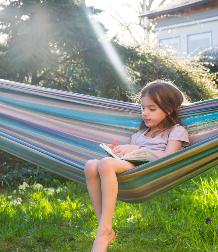 Little girl sitting on hammock in the garden reading a book