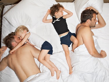 Two man with their two children sleeping in the bed covered in white sheets. 