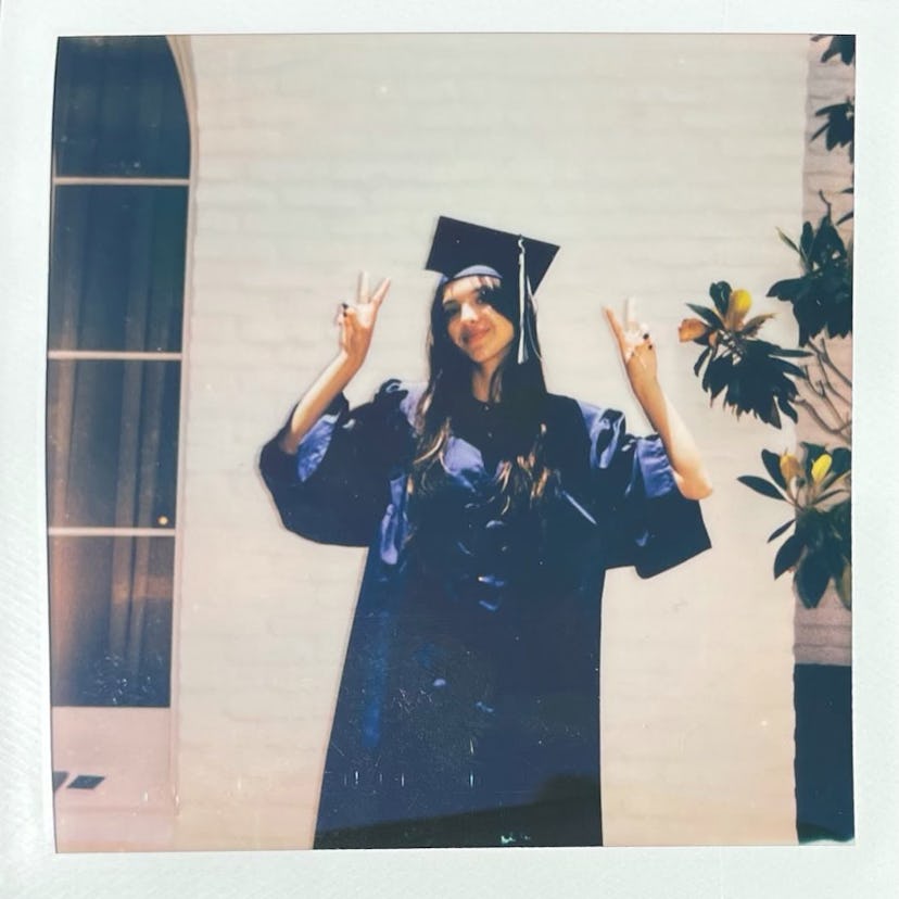 Olivia Rodrigo waves two peace signs in the air while dressed in a graduation cap and gown.