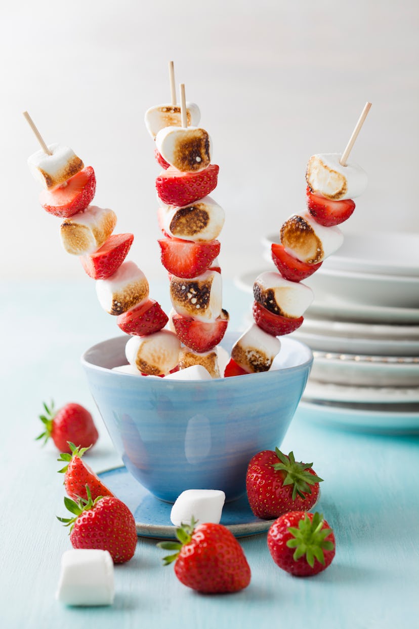 Blue bowl with skewers of strawberries and toasted marshmallows coming out of it