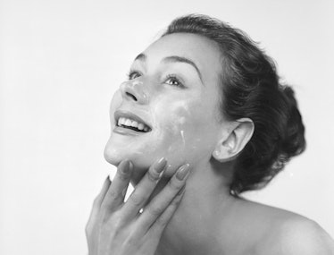 A model applying a face cream while smiling.  