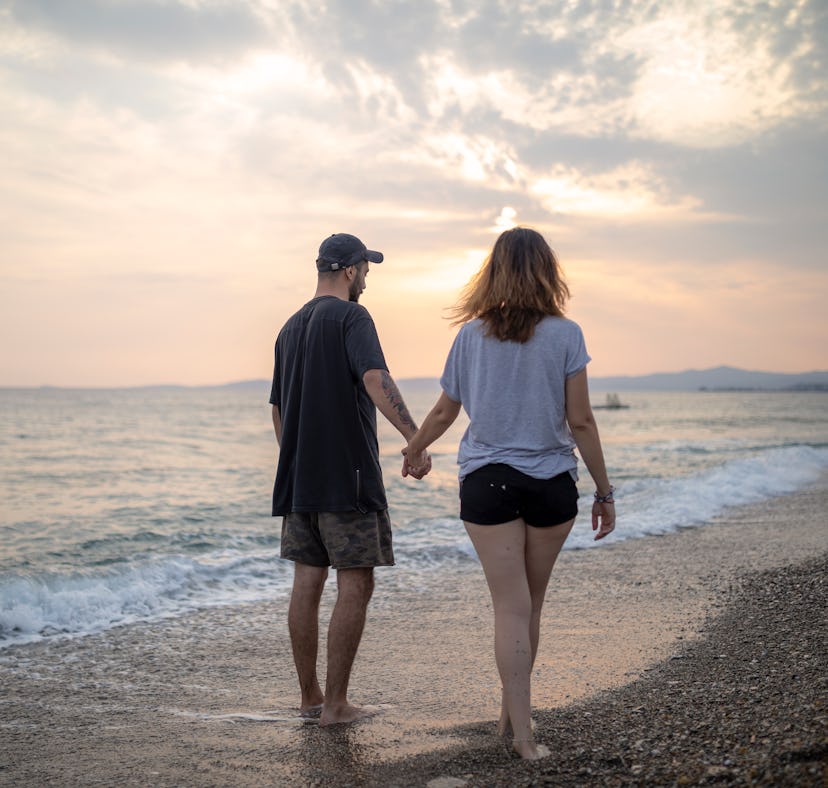 Young couple holding hands while walking the beach at night, ready to post a pic on Instagram with a...