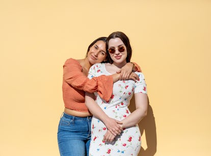 Young woman hugging her little sister, posing for a picture before posting on Instagram with little ...