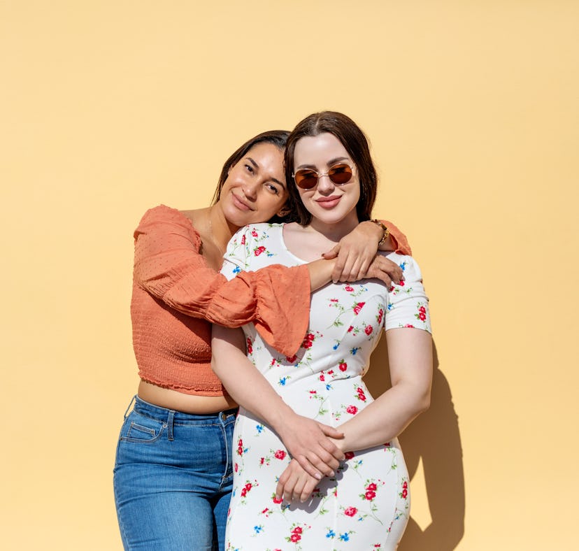 Young woman hugging her little sister, posing for a picture before posting on Instagram with little ...