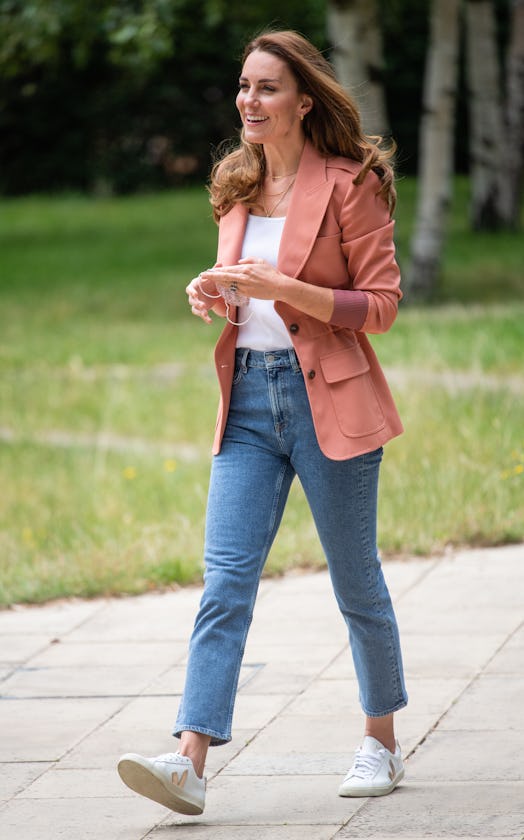 Catherine, Duchess of Cambridge wears white Veja sneakers, blue jeans, and a pink blazer while visit...