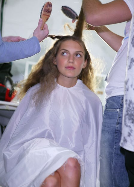 A wavy-haired girl has her hair combed and styled by two people. 