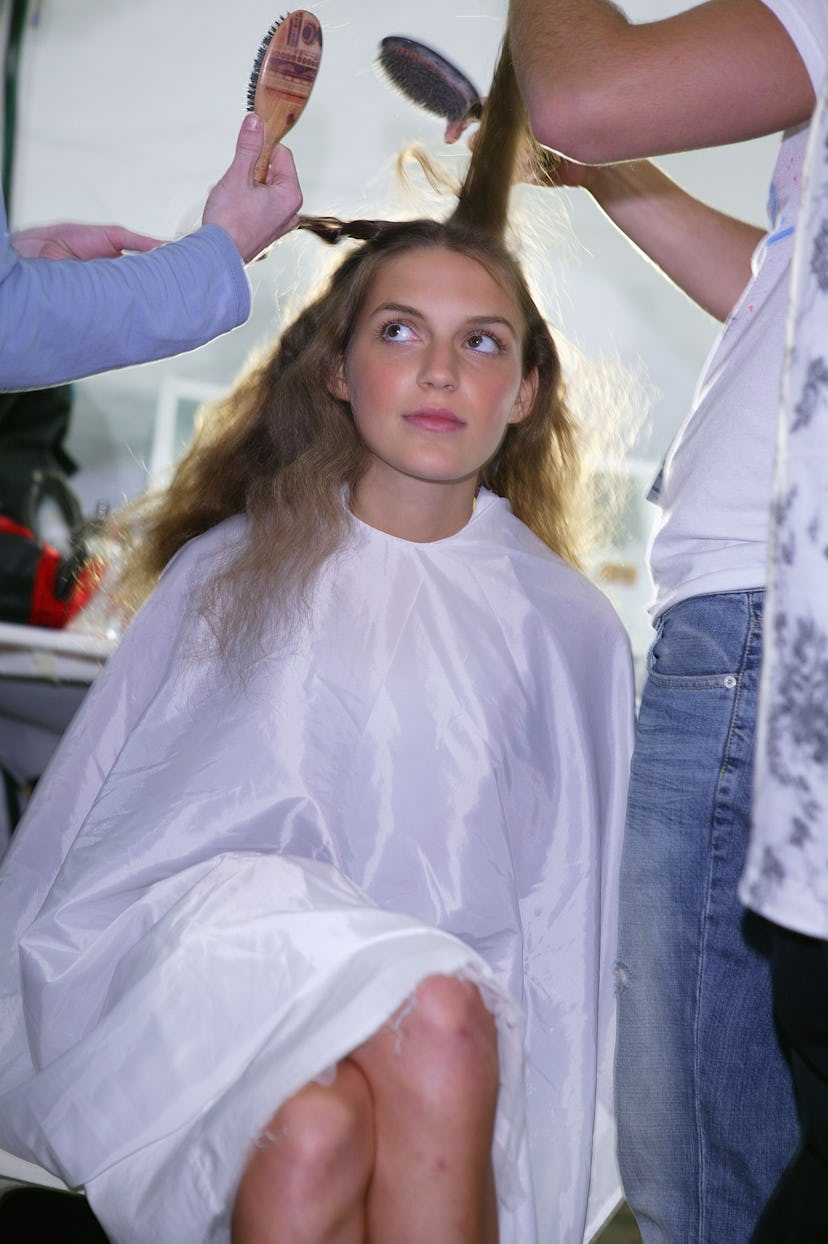 A wavy-haired girl has her hair combed and styled by two people. 