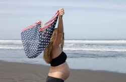 pregnant woman on beach, holding American Flag print scarf 