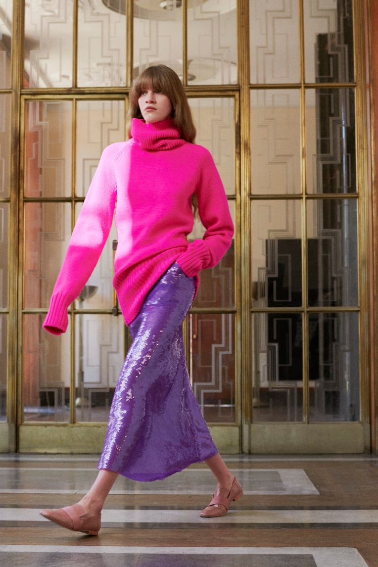 Model walking while wearing a pink sweater and a purple sequin skirt