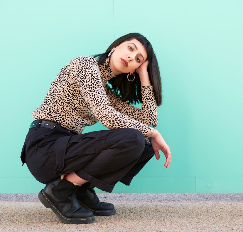 Young woman crouching on the floor in front of a blue wall, feeling bad during the month of July 202...