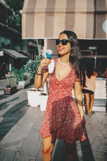 Young woman wearing sunglasses and a summer dress holding an ice cream cone before posting a pic on ...
