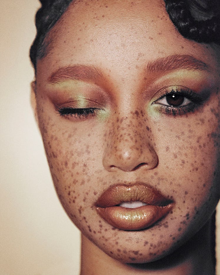 A model with freckles, closing one eye and showing off her bronze and green eyeshadow 