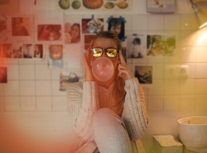 Young woman wearing sunglasses, blowing a bubble before posting a pic on Instagram with a sweet gum,...